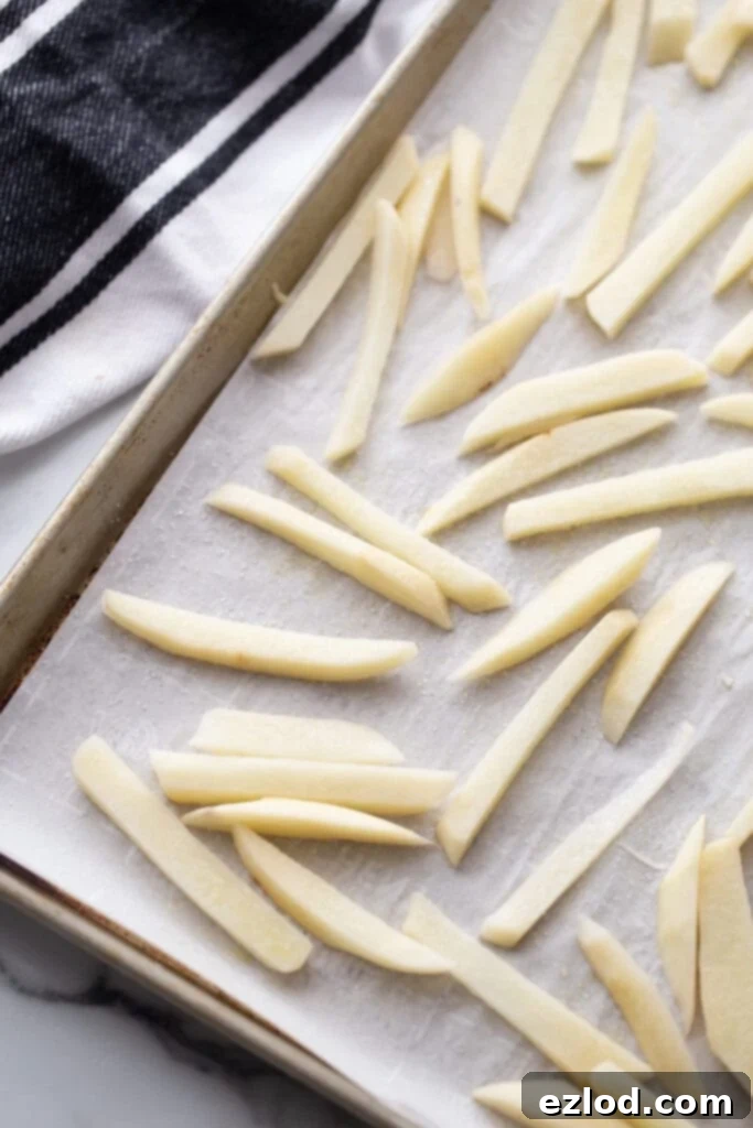 Overhead photo of a parchment lined sheet pan with fries, ready to make baked French fries.