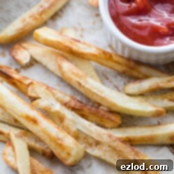 Homemade Fries Anytime: The Freezer Secret 10 Overhead photo of golden brown homemade baked French Fries on a parchment lined sheet pan. There is a white ramekin of ketchup on the corner of the pan.