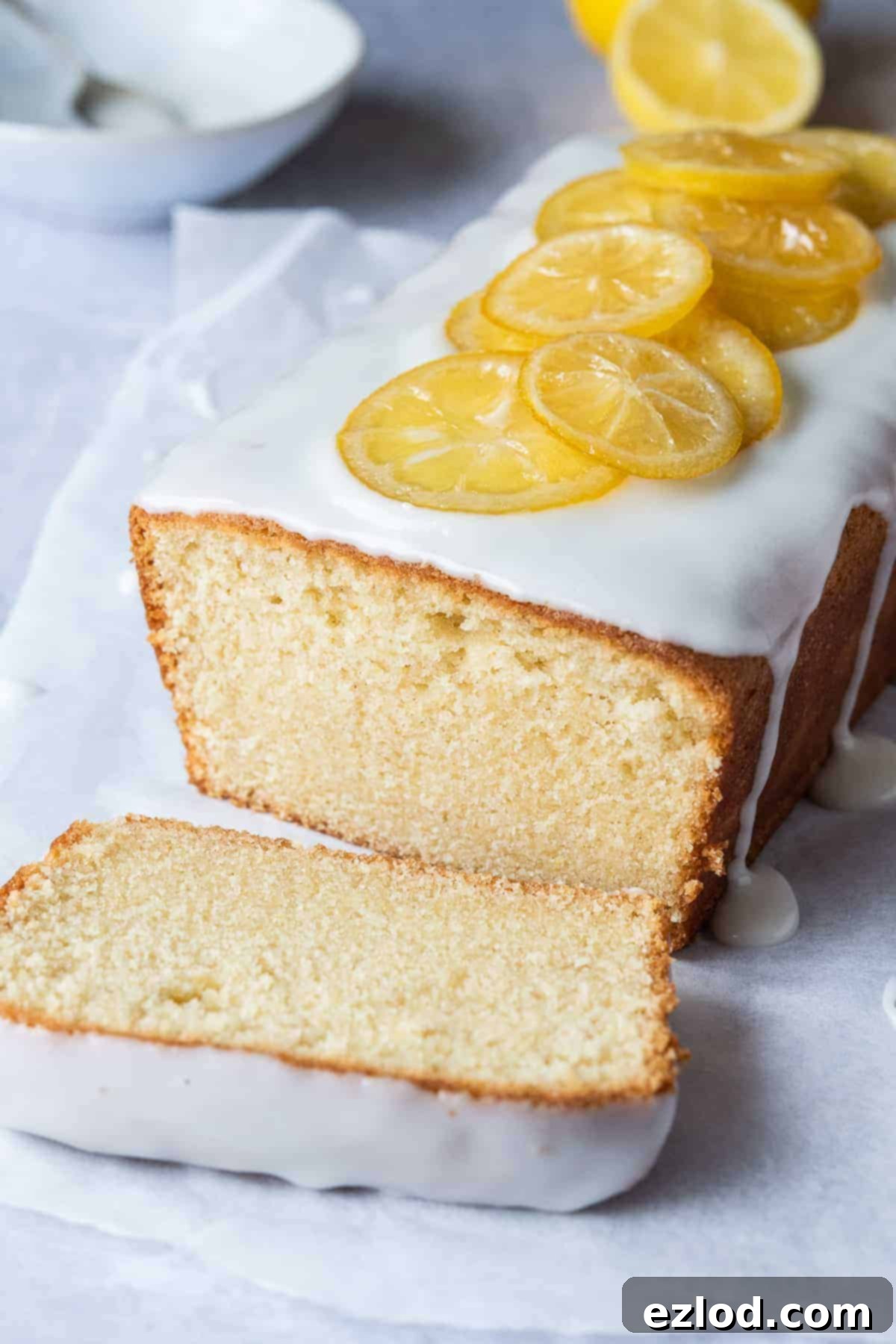 A beautifully baked loaf of vegan lemon pound cake with one perfect slice cut and presented on white baking parchment, emphasizing its moist interior.