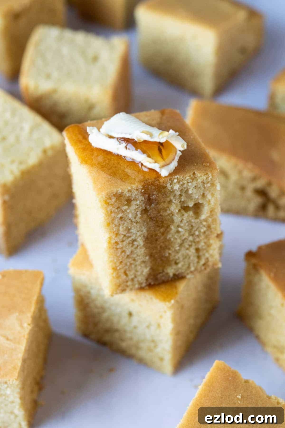 A stack of two squares of easy vegan cornbread topped with butter and maple syrup, showcasing its golden-brown crust and fluffy interior.