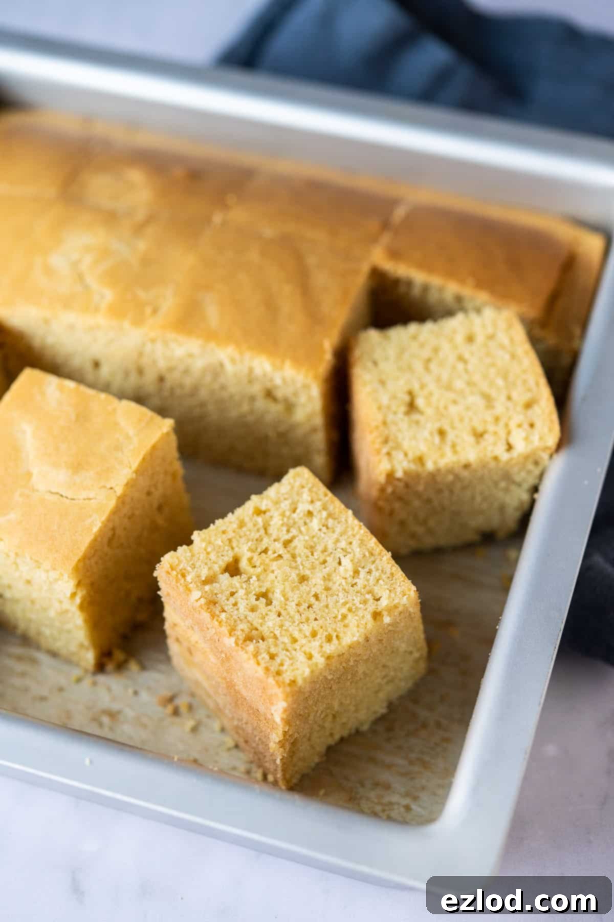 Several golden-brown squares of vegan cornbread arranged neatly in a metal cake tin, ready for serving.