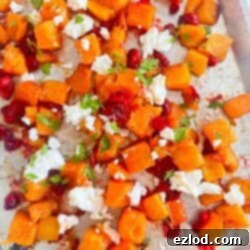 Sheet pan with roasted butternut squash and cranberries topped with goat cheese and fresh parsley.