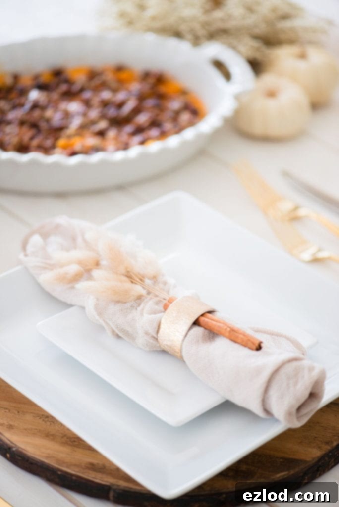 White casserole dish with a 21 day fix healthy sweet potato casserole topped with pecans on a white wooden table set in the background. In the foreground is a Thanksgiving style place setting. 