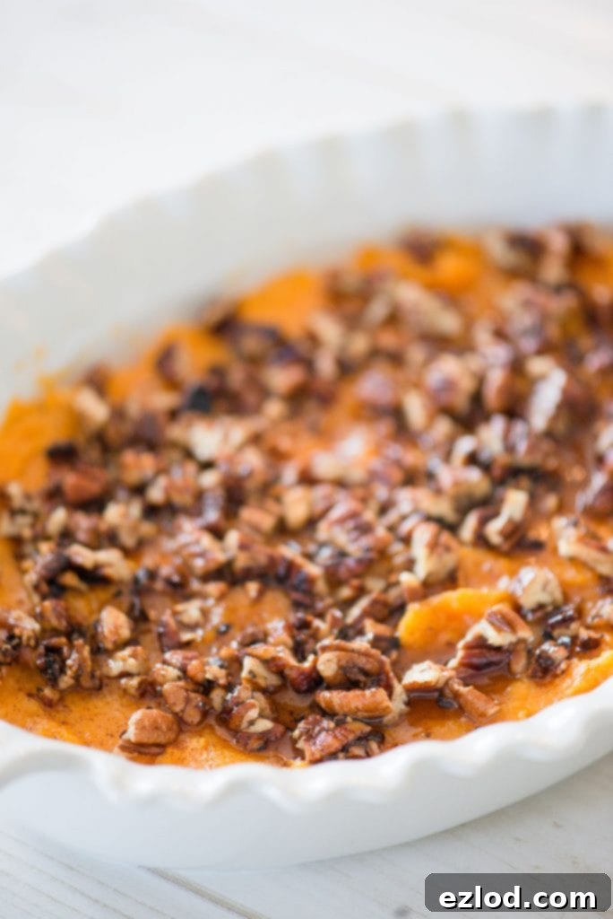 White casserole dish with a healthy sweet potato casserole topped with pecans on a white wooden table. 