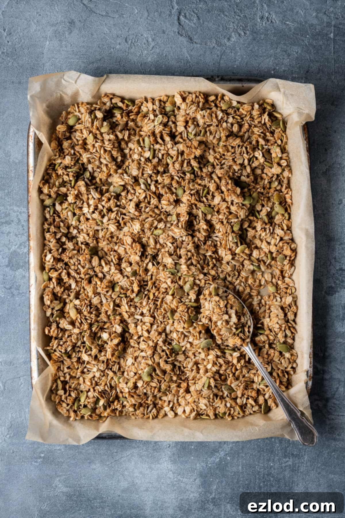 Golden vegan granola cooling on a parchment-lined baking tray on a grey background.