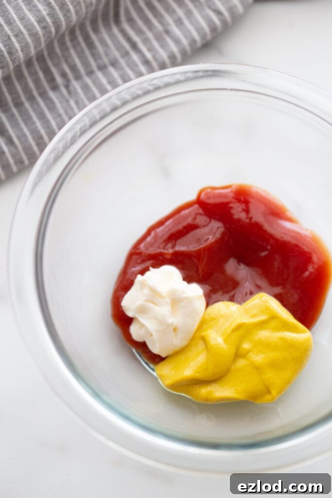 Ingredients for the best burger sauce- ketchup, mustard, and mayo- in a glass bowl with a gray and white striped kitchen towel off to the side.