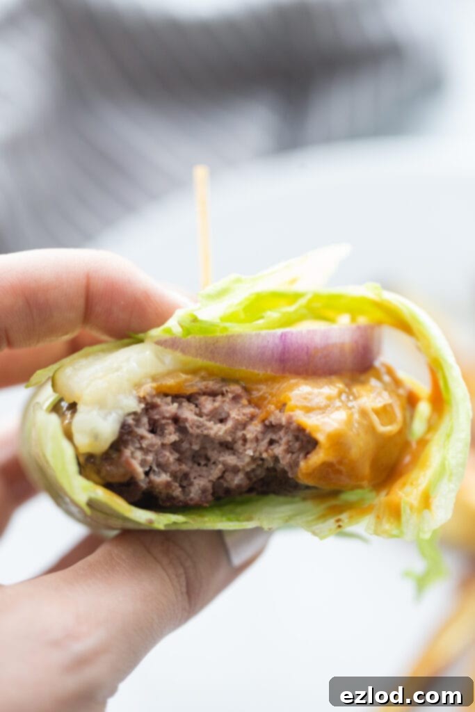 Close up photo of a lettuce wrapped burger topped with cheddar cheese, burger sauce, red onion, and pickles, all held together with a toothpick sticking out of the center.