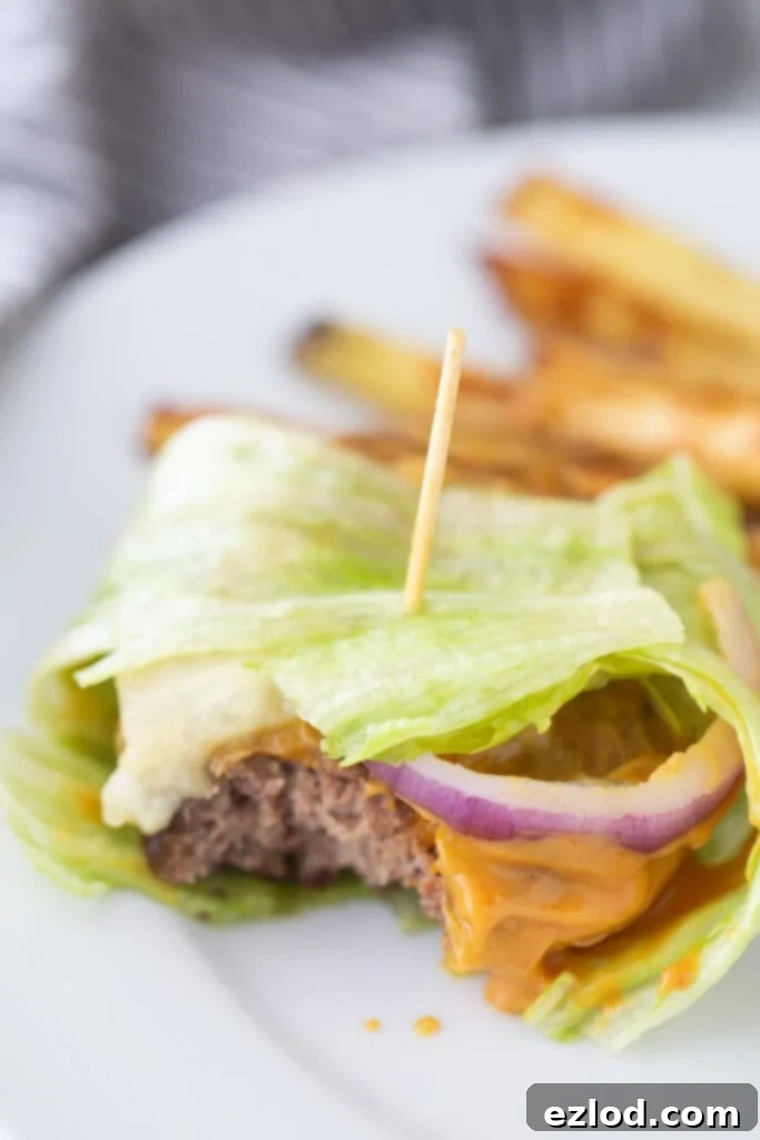 A toothpick is holding together a lettuce wrapped burger with delicious toppings and burger sauce, with homemade french fries in the background.
