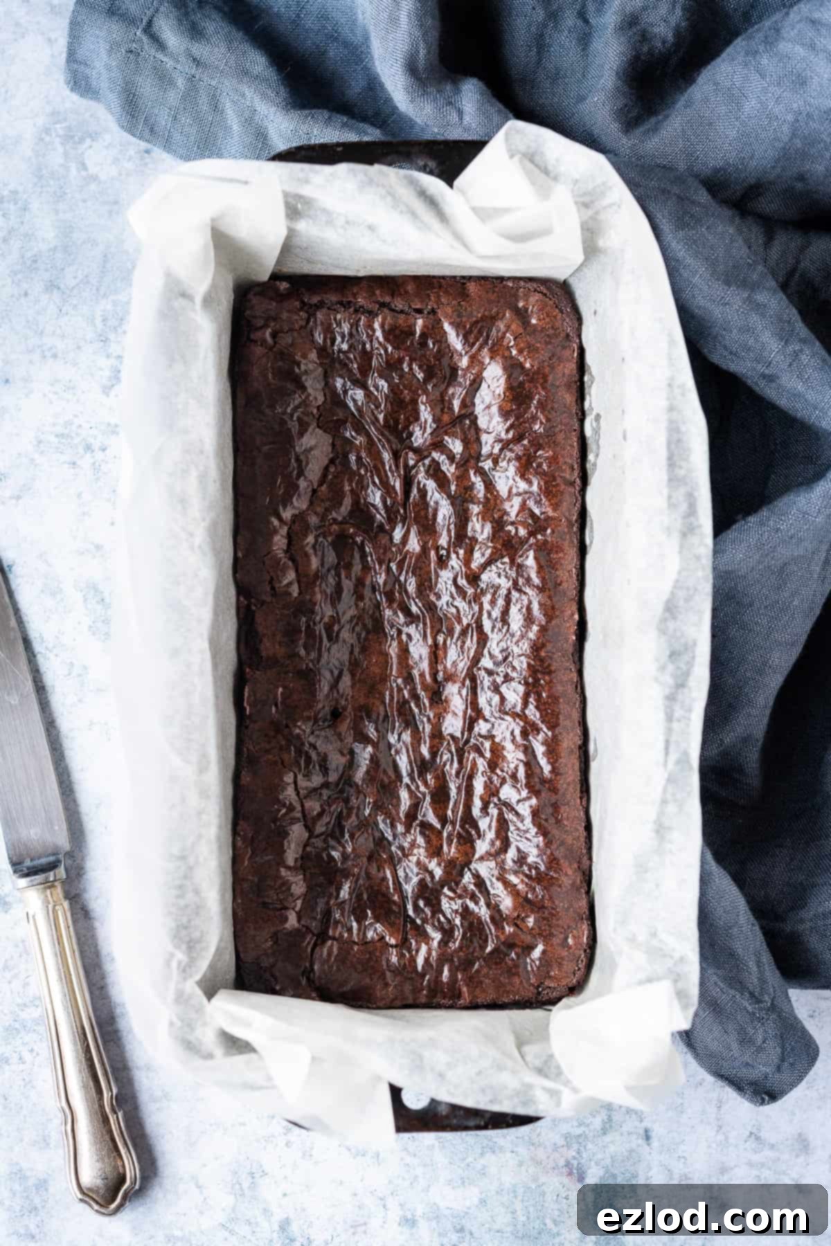 Freshly baked small batch vegan brownies, still warm, resting beautifully in a loaf pan, showcasing their rich, dark crust and inviting texture.