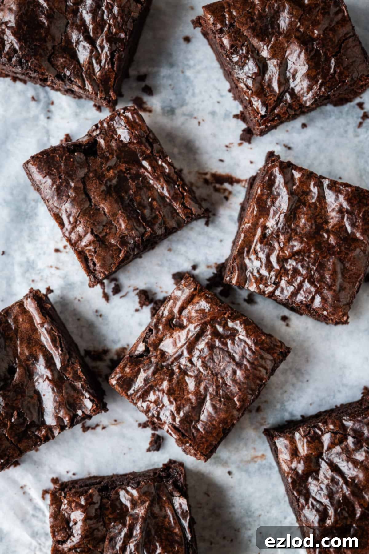 Eight perfectly square portions of rich, fudgy vegan brownies artfully arranged on crisp white baking parchment.