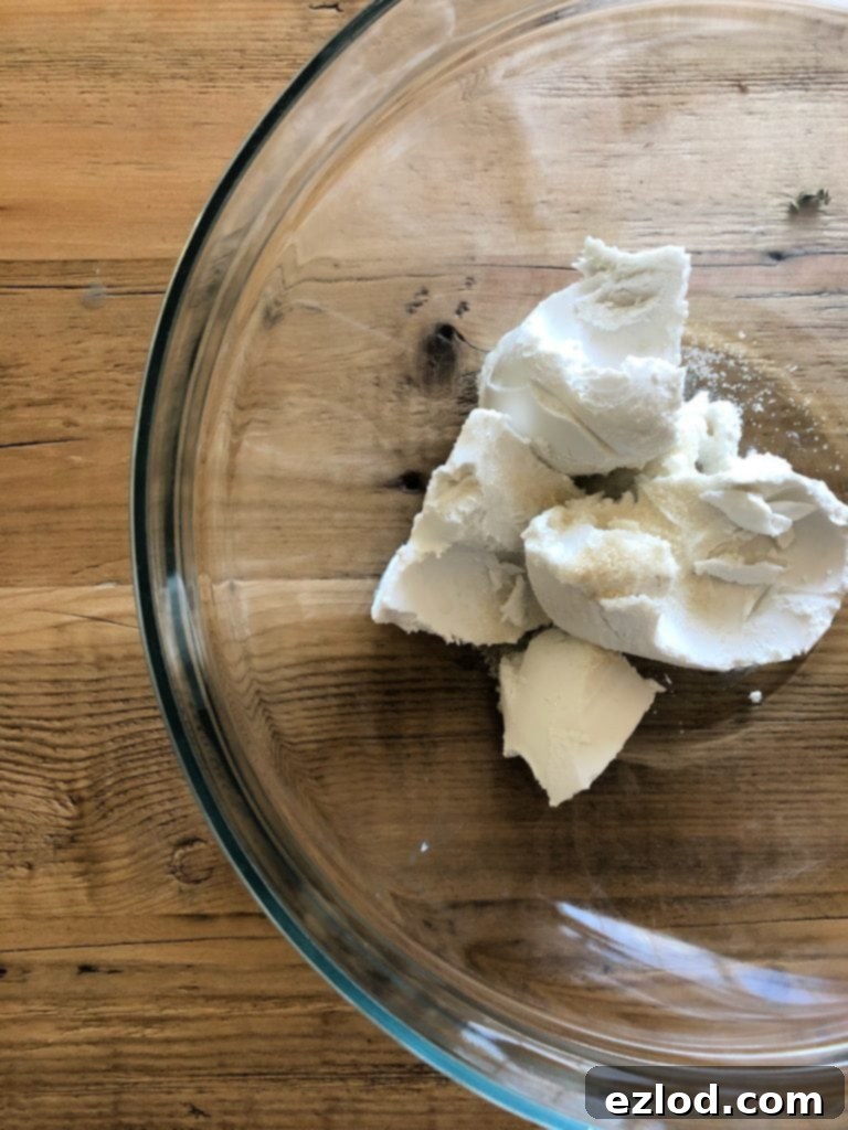 A glass bowl filled with thick, white coconut cream is ready for whipping, set on a rustic wooden table.