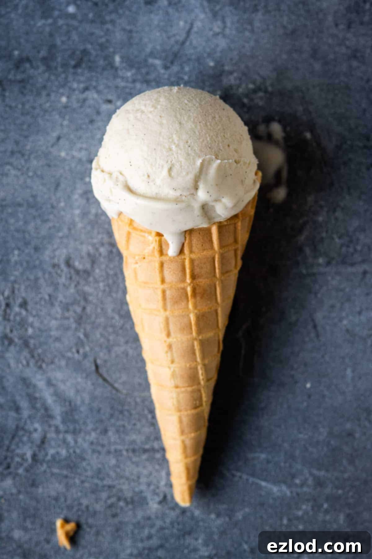A waffle cone with a single scoop of vegan vanilla ice cream on a grey background.