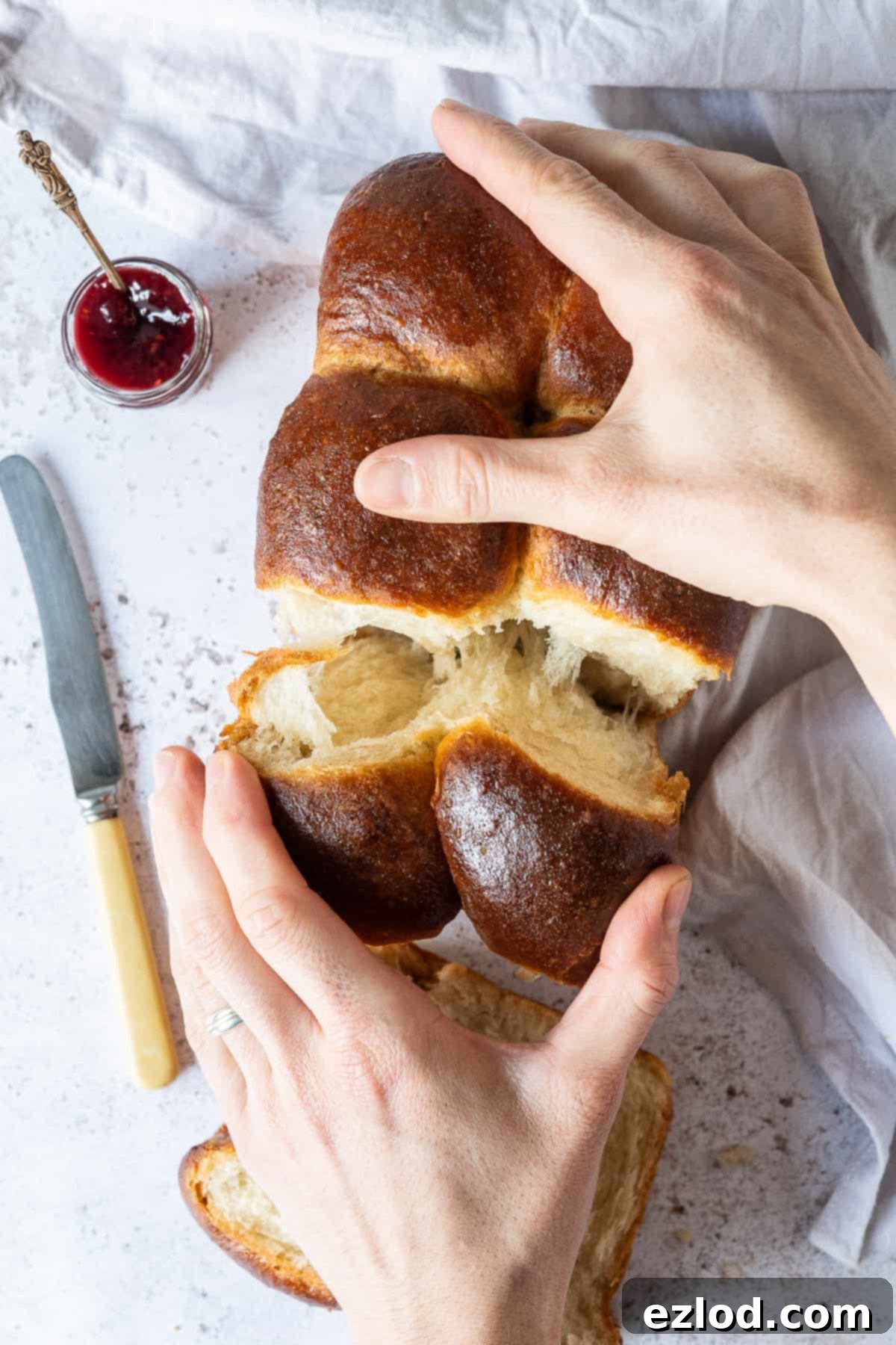 A loaf of brioche being torn apart by hands.