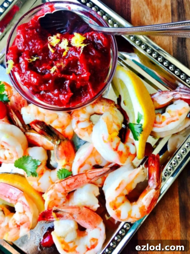 Cooked shrimp on a silver platter with cranberry horseradish sauce in a small glass bowl on the corner of the platter.