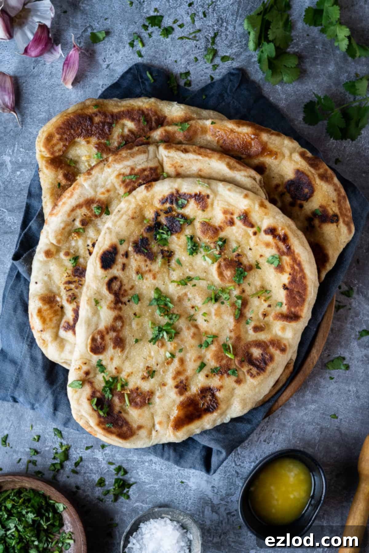 four vegan naan breads on a grey cloth on a dark grey background with garlic, coriander, salt and garlic butter.