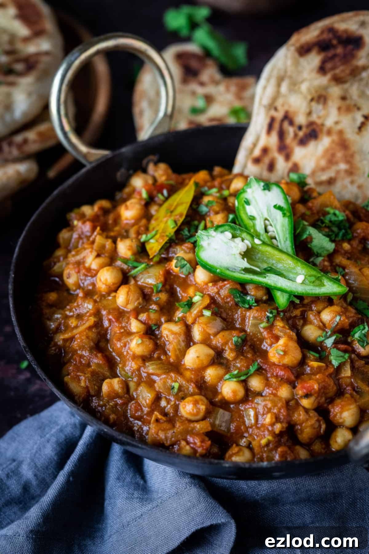 Close up of a black metal dish of chana masala topped with green chillies and coriander.