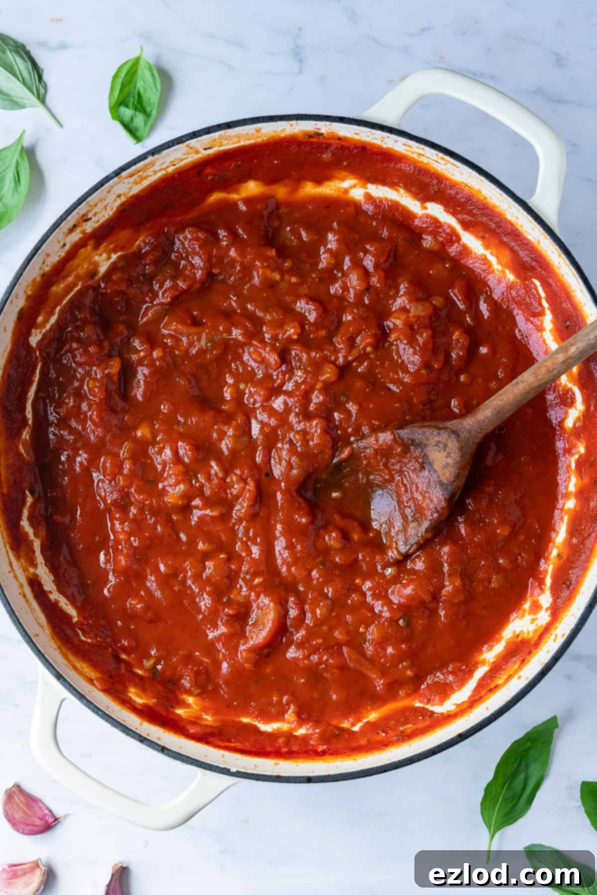Close-up of a bubbling, rich red marinara pasta sauce simmering in a black pan with fresh basil.