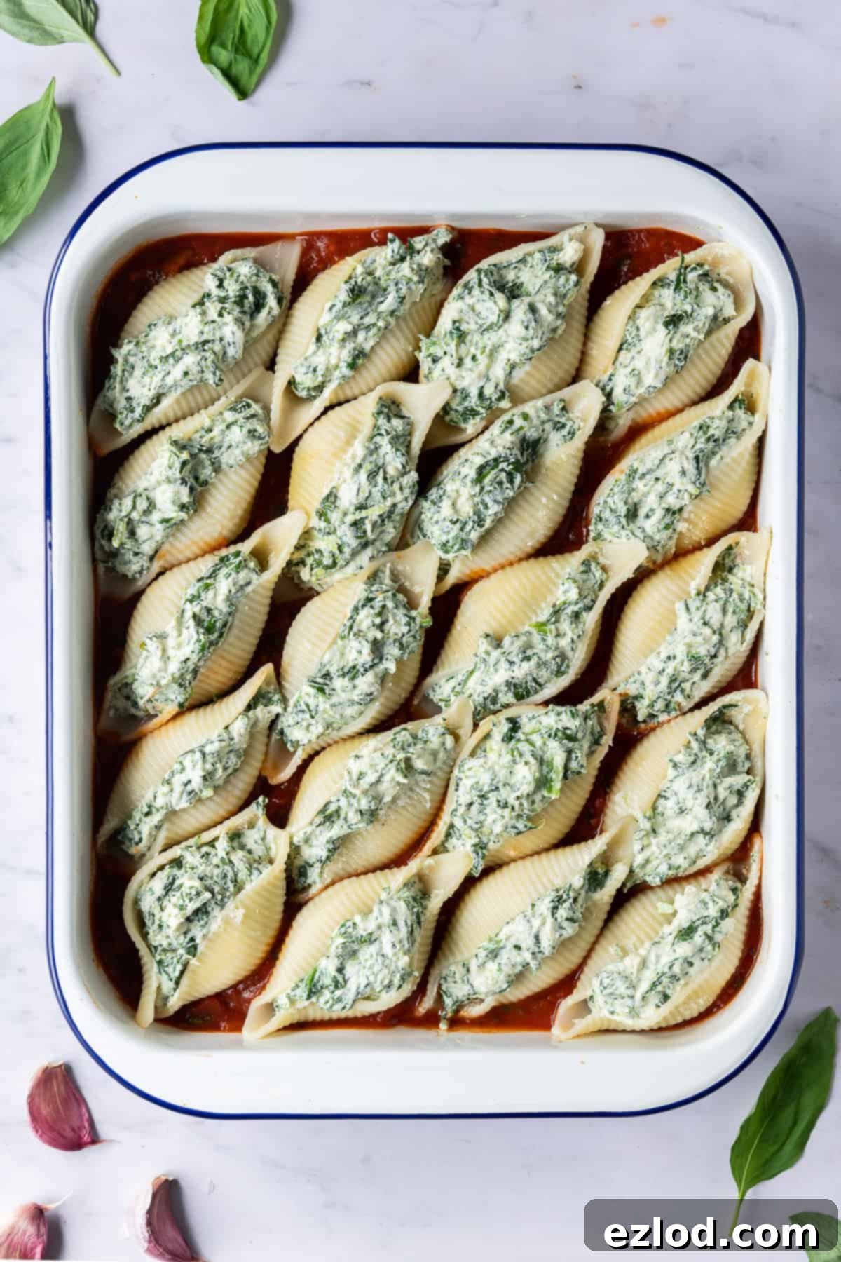 Unbaked vegan spinach and ricotta stuffed pasta shells neatly arranged in a white baking dish on a bed of marinara sauce, ready for the oven.