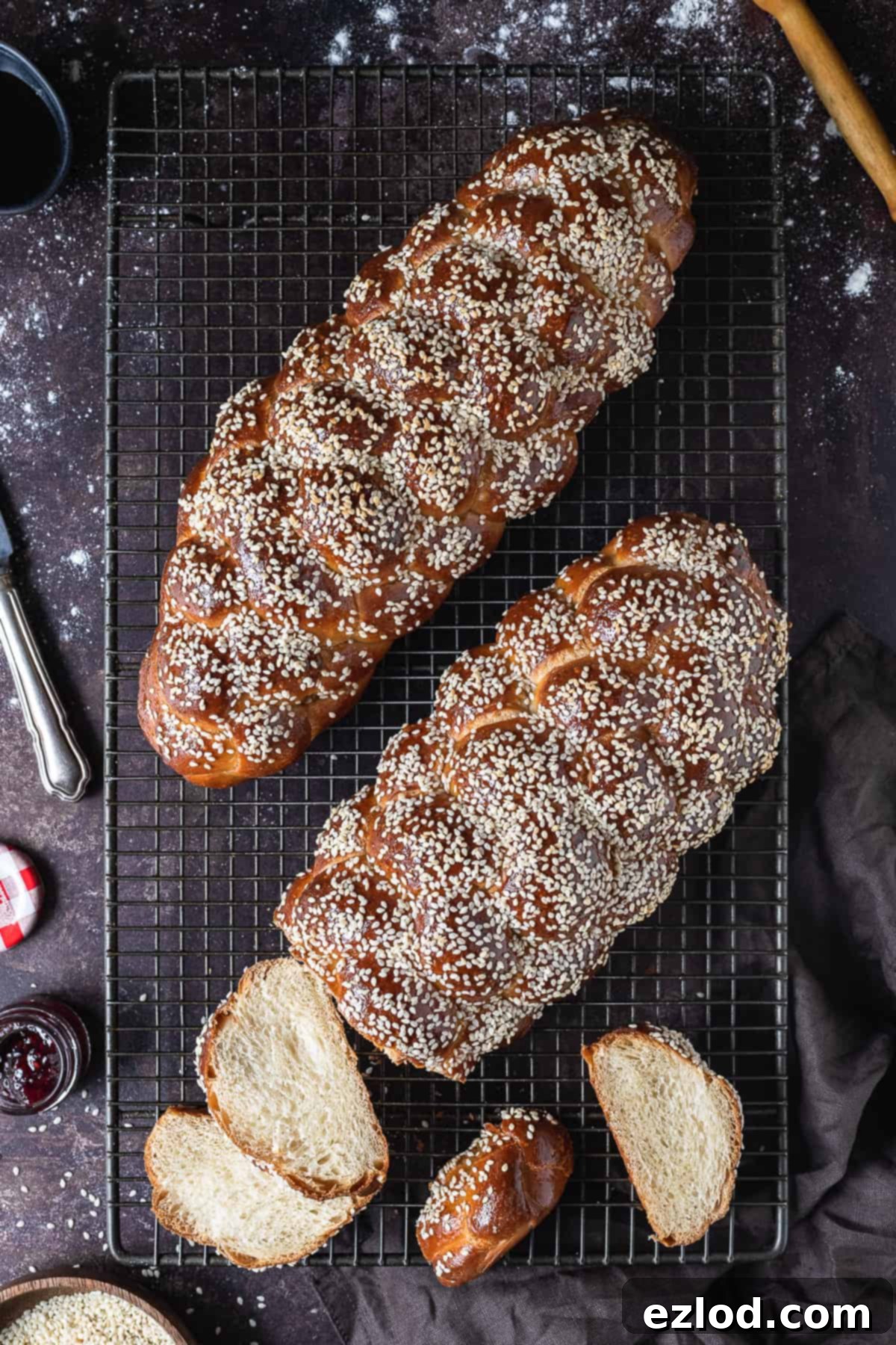 Two freshly baked loaves of golden-brown vegan challah, beautifully braided and topped with sesame seeds, cooling on a wire rack after being glazed and baked.
