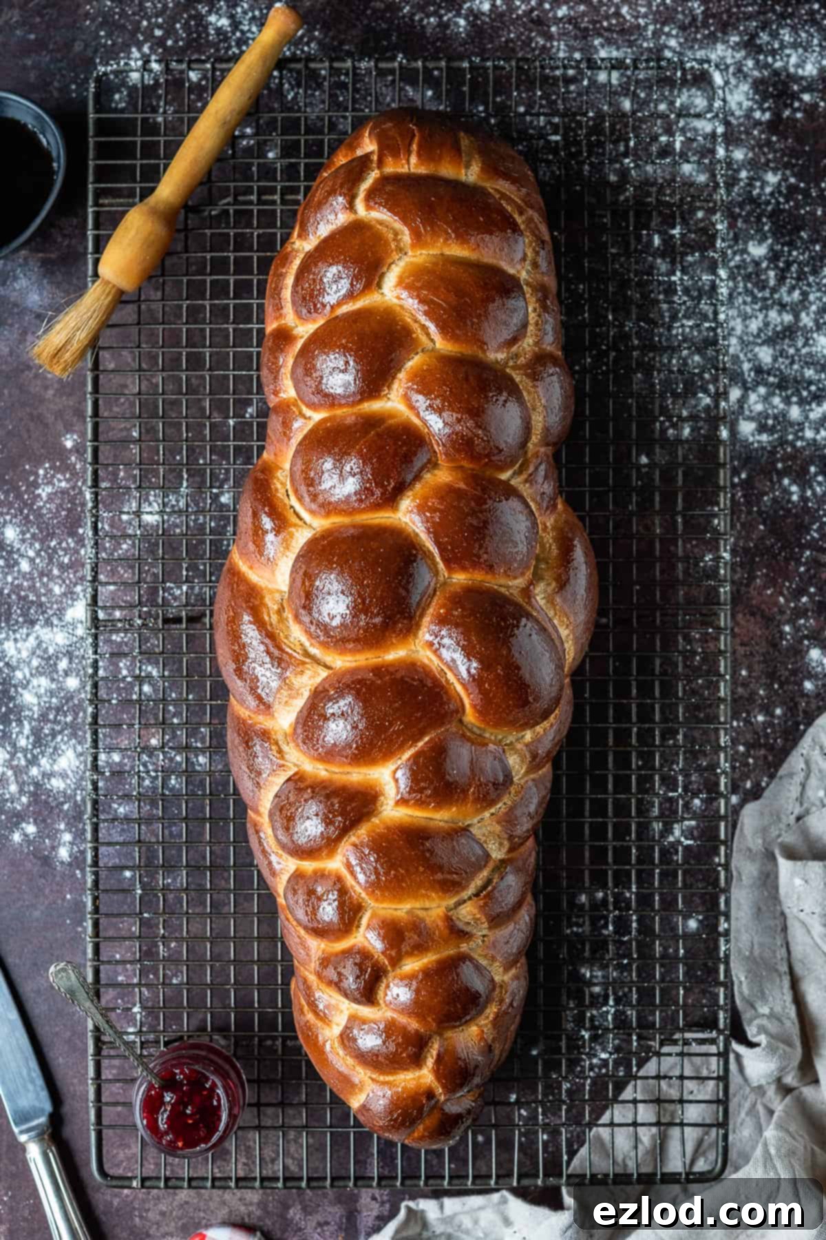 A beautifully braided loaf of golden-brown vegan challah bread resting on a dark, textured background, showcasing its intricate pattern and appealing crust.