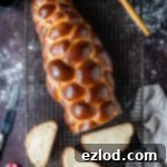 Sliced vegan challah bread on a wire cooling rack on a dark background with a cloth, pot of jam and a pastry brush, highlighting its soft crumb.