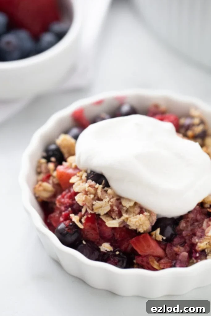A detailed close-up shot of an individual serving of mixed berry crisp, lusciously topped with a dollop of fluffy, homemade coconut cream. The rich textures and inviting colors promise a delightful and healthy dessert experience.