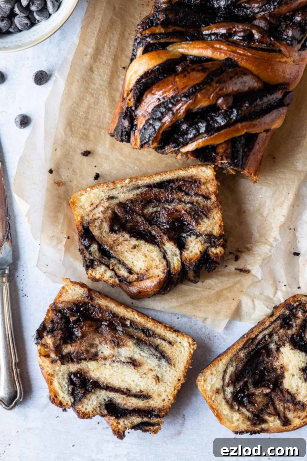 A perfectly sliced vegan chocolate babka showcasing its beautiful chocolate swirls, resting on brown baking parchment on a subtle grey background.