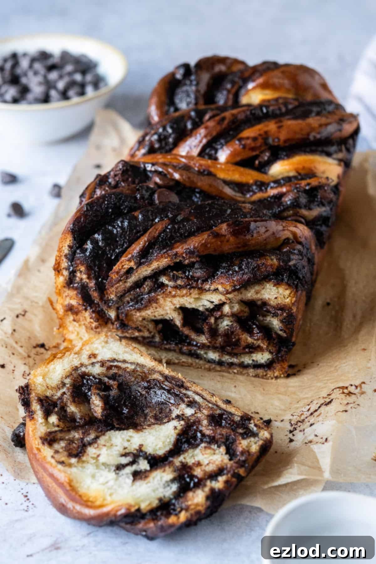 A whole vegan chocolate babka loaf on a sheet of brown baking parchment, ready to be sliced and enjoyed.