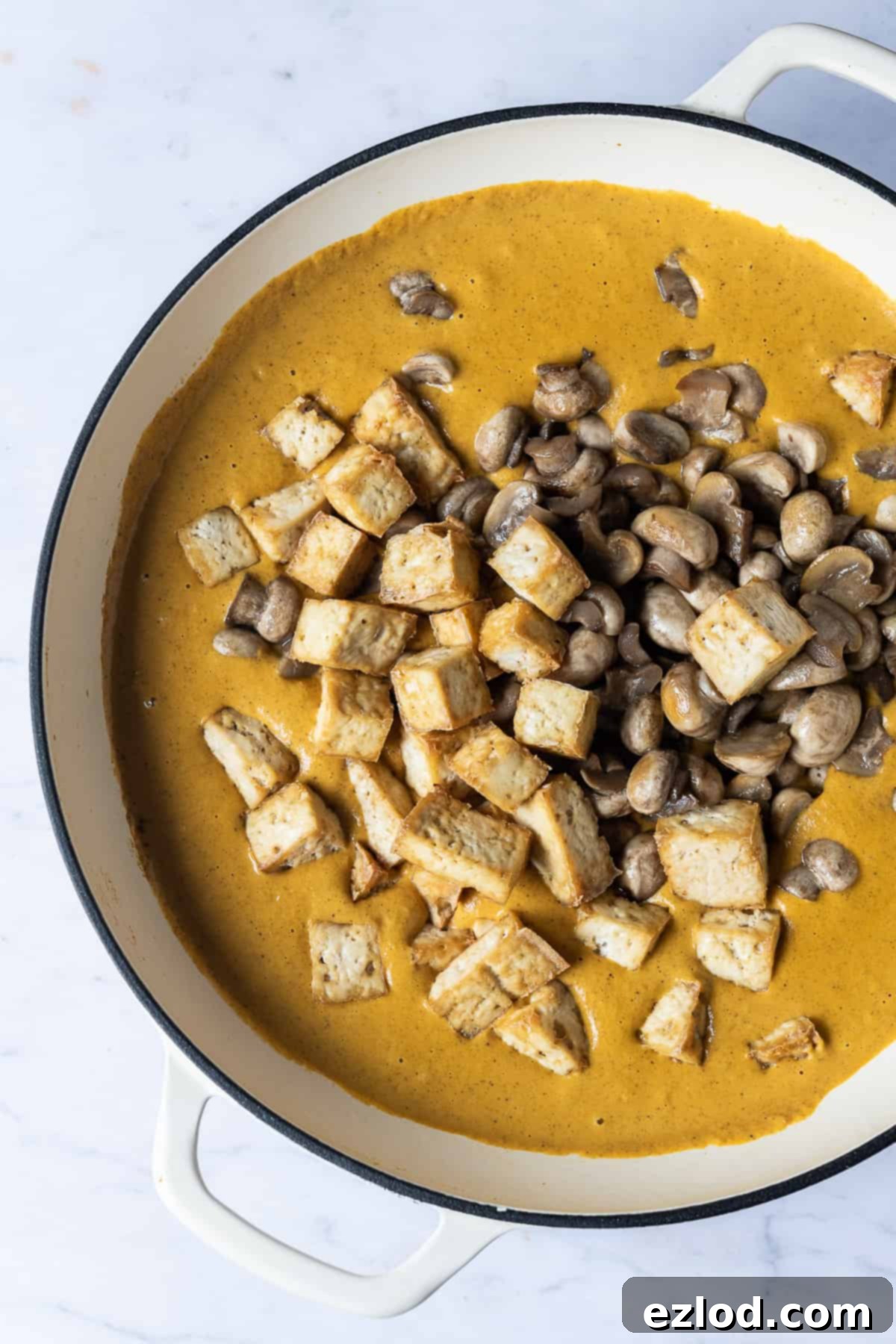 Vegan korma sauce in a white pan topped with tofu and fried mushrooms.