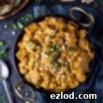 Vegan mushroom and tofu korma in a black karahi pan on a dark background with chopped cahews, coriander and naan breads.