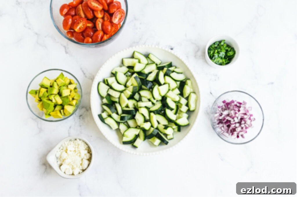 Individual white and clear bowls of ingredients to make cucumber tomato salad on a white background.