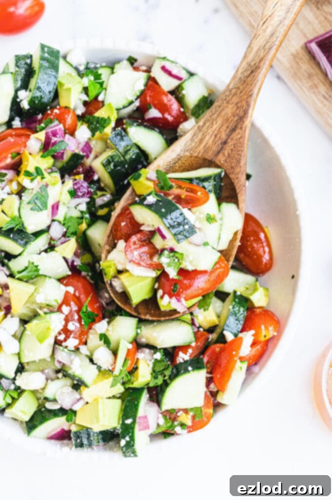 Overhead photo of chopped cucumber tomato salad in a large serving bowl with a wooden spoon.