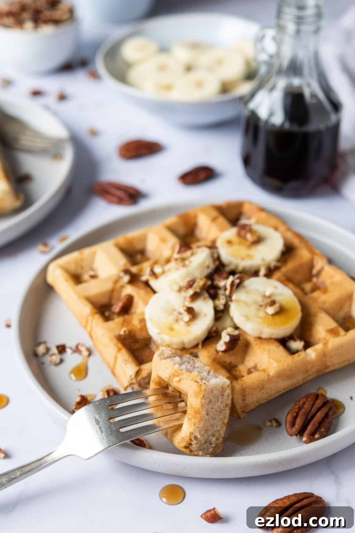 A single vegan banana waffle on a grey plate with a forkful removed, showing its fluffy interior.