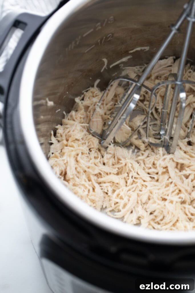 Instant Pot filled with cooked, shredded chicken and mixer blades, illustrating quick shredding.