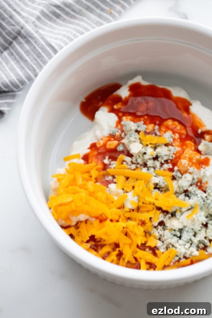 Casserole dish filled with cottage cheese, blue cheese, cheddar cheese, and hot sauce, ready to be mixed into a creamy buffalo chicken dip base.