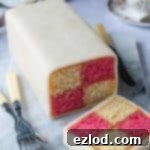 A beautifully presented vegan Battenberg cake resting on a sleek marble board, set against a subtle grey background.