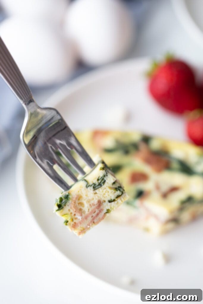 A close-up of a bite of baked eggs with spinach and bacon on a fork, showing the texture and deliciousness.