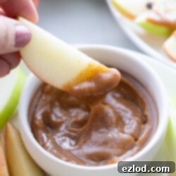 A small glass bowl of vegan caramel dip with a spoon, surrounded by apple slices, ready to be enjoyed.