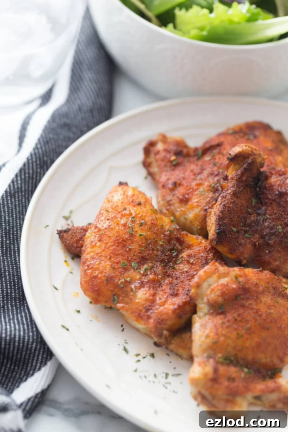 Effortless Crispy Chicken Thighs 5 Overlapping pieces of air fryer chicken thighs on white plate.