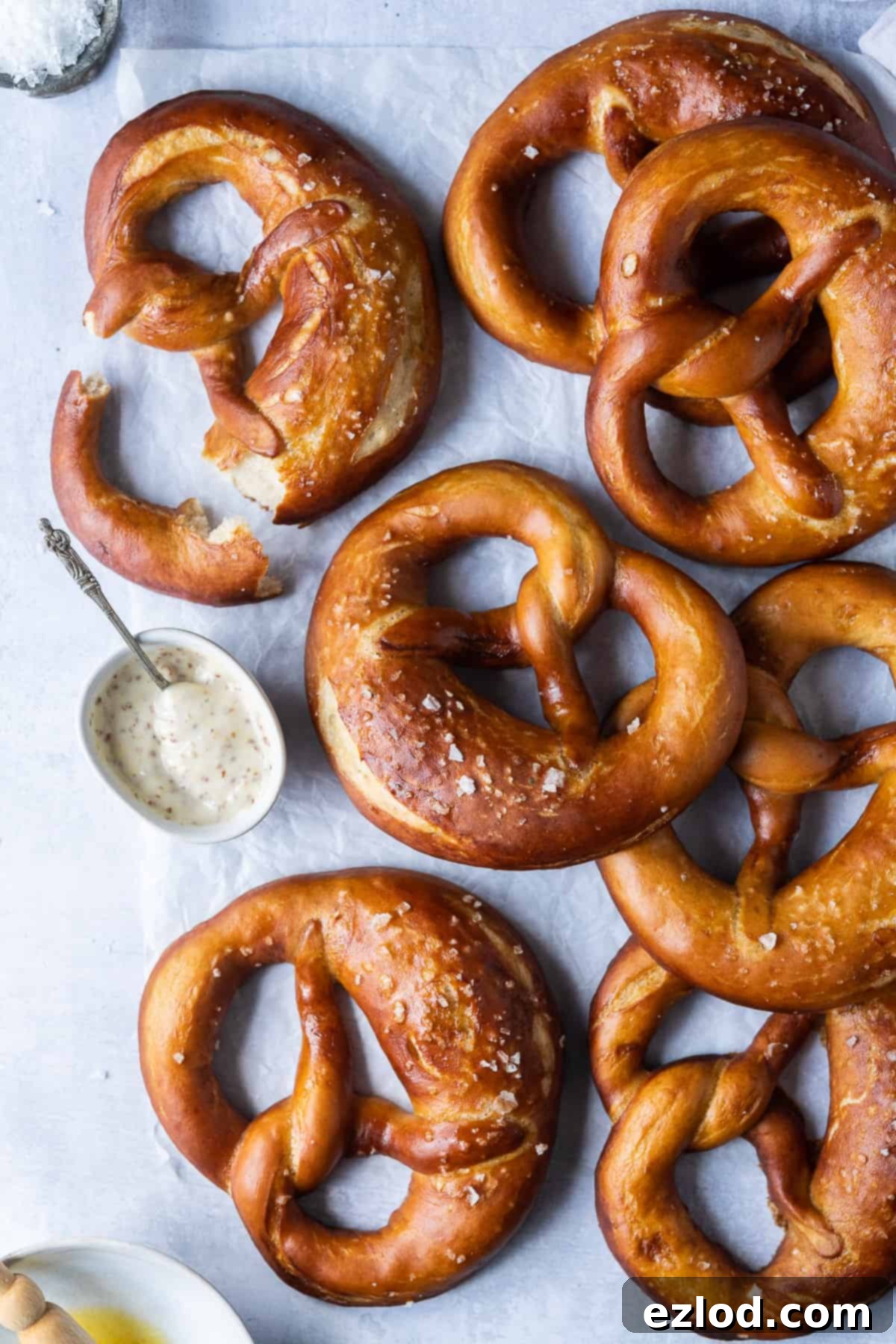 Freshly baked vegan beer pretzels arranged on a sheet of white baking parchment next to a small bowl of tangy mustard dipping sauce, highlighting their golden-brown crust and classic knot shape.