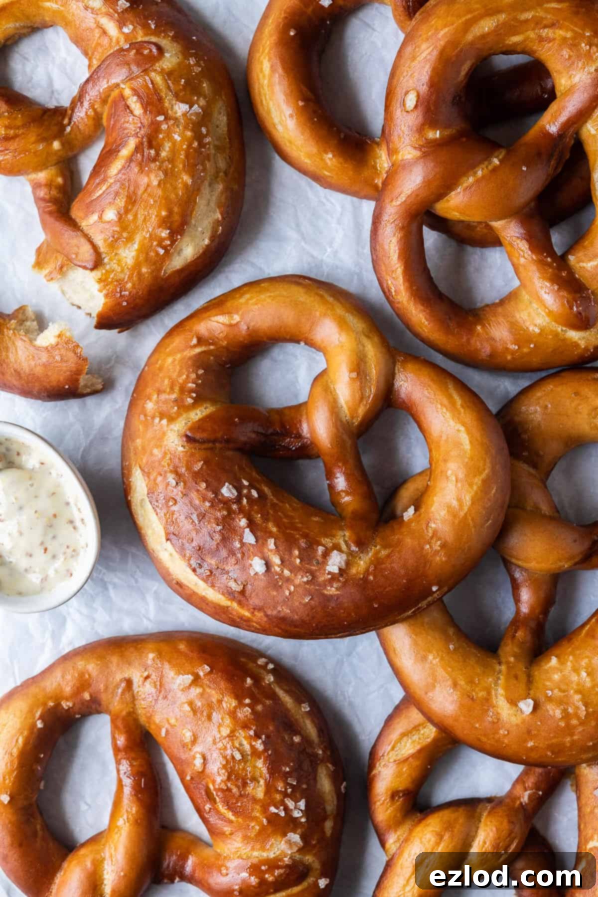 A batch of perfectly baked vegan beer pretzels, golden brown and sprinkled with salt, resting on a sheet of white baking parchment, ready to be enjoyed.