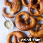 Vegan beer pretzels on a sheet of white baking parchment with a bowl of mustard sauce.