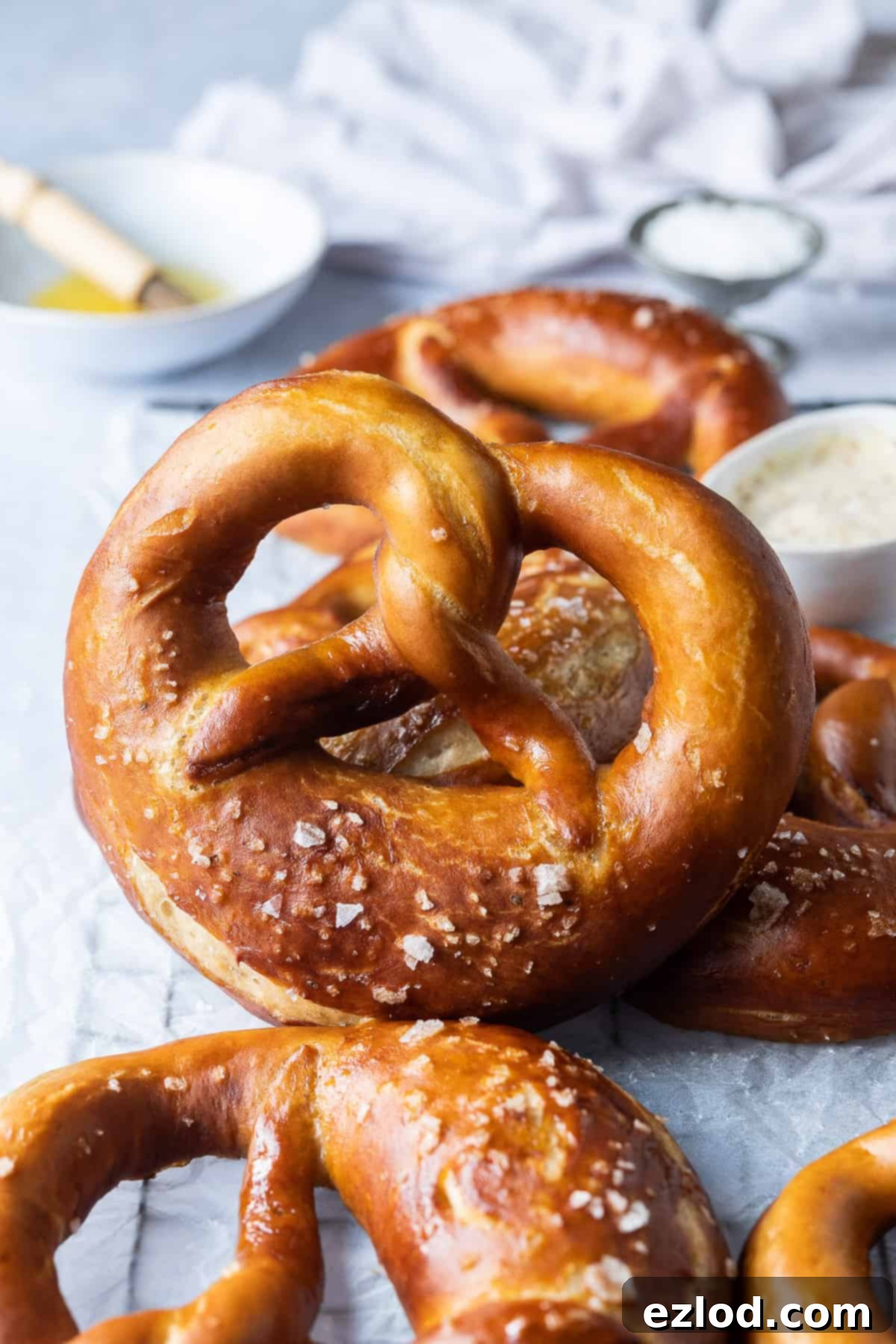 Close-up shot of a perfectly baked vegan beer pretzel cooling on a wire rack, with a small bowl of melted vegan butter and a pastry brush in the background, ready for a final glaze.