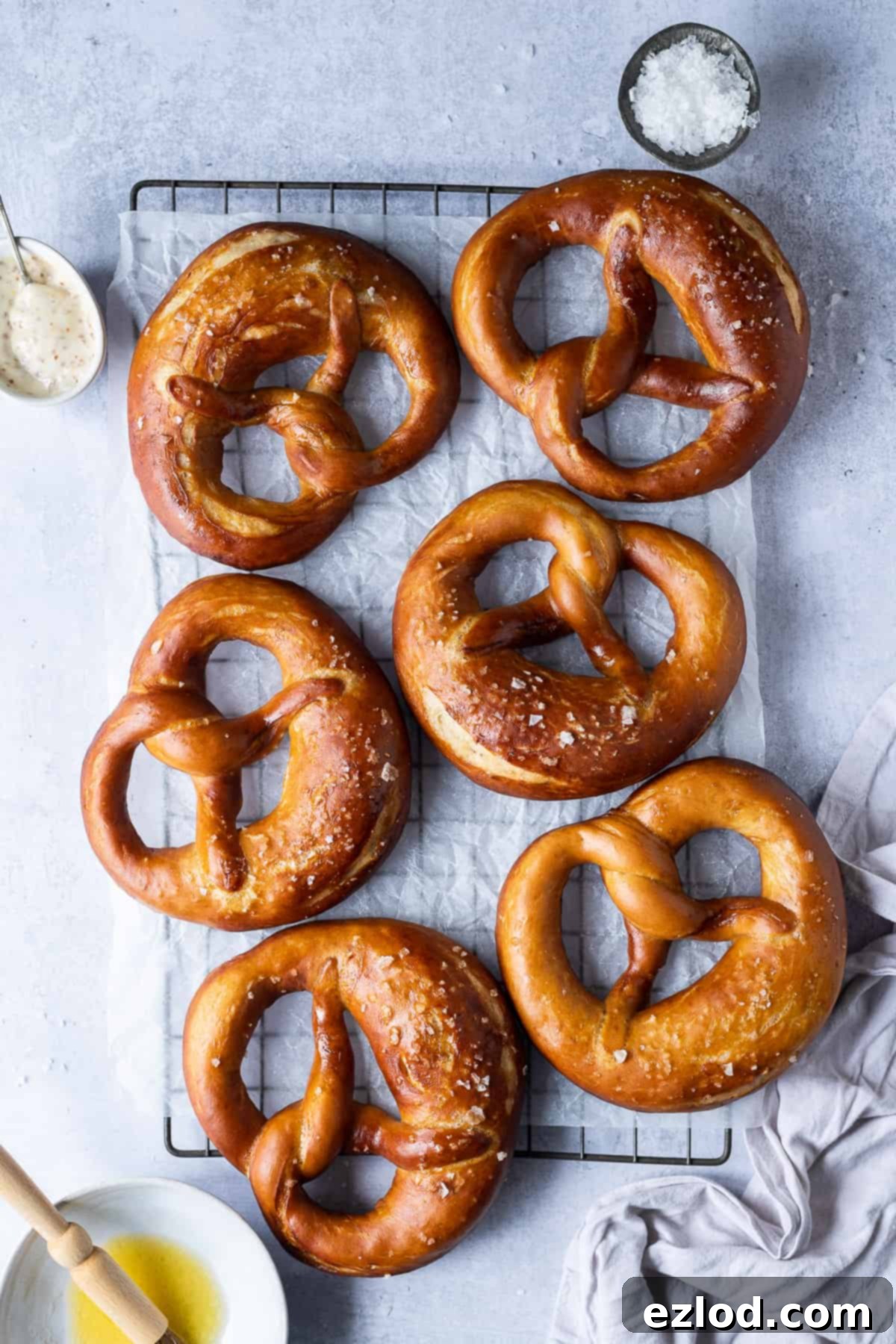 A collection of beautifully golden-brown vegan pretzels cooling on a wire rack against a soft grey background, showcasing their perfect shape and inviting texture.
