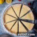 Sliced vegan lemon tart on a grey background with lemons and raspberries.