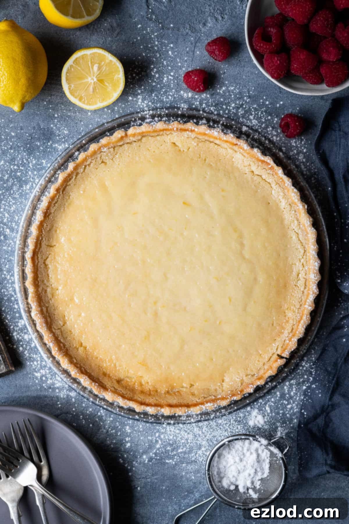 Vegan tarte au citron on a grey background with lemons and raspberries, ready to be served.