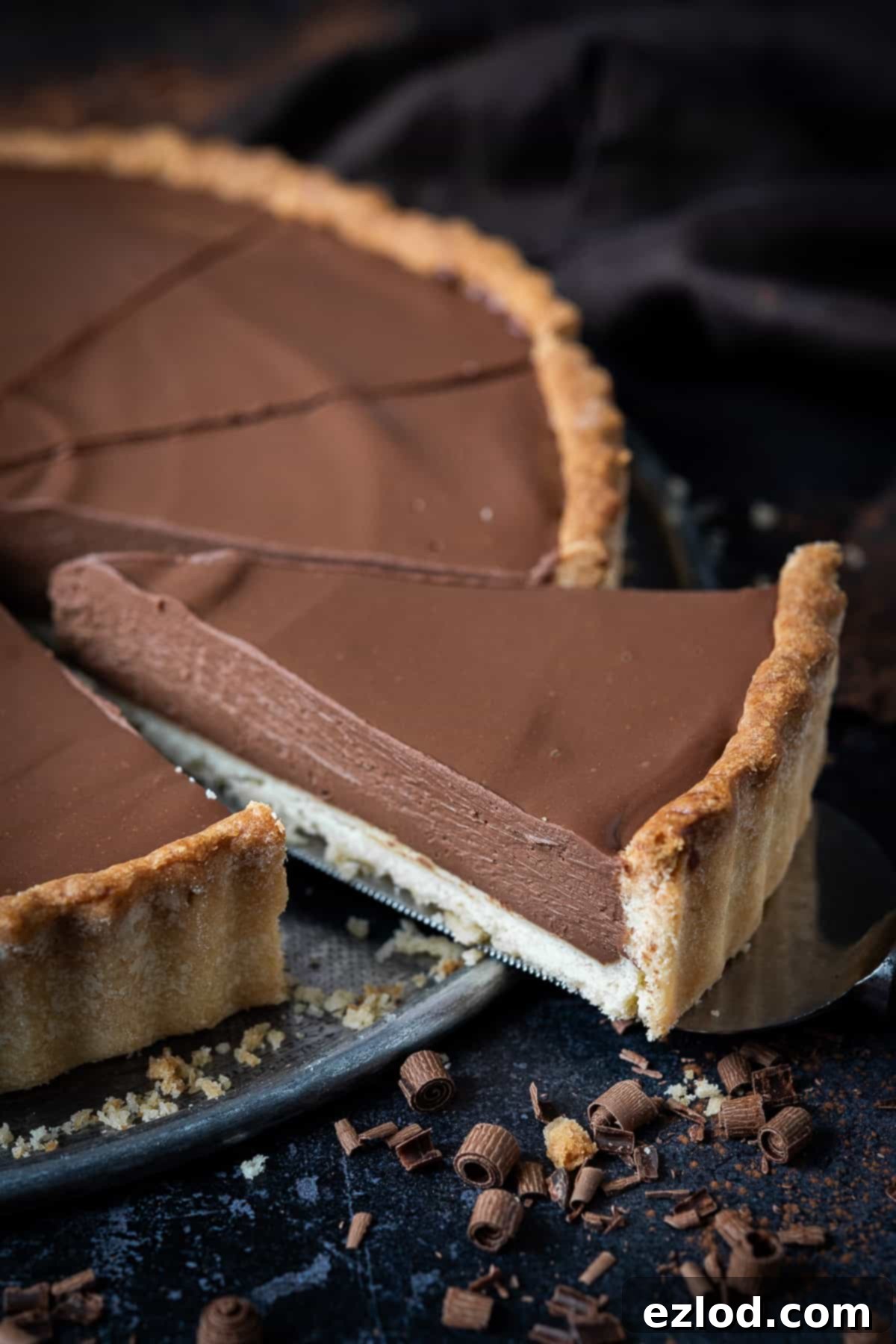 A close-up view of a perfectly cut slice of vegan peanut butter chocolate tart, showcasing its smooth filling and flaky crust.