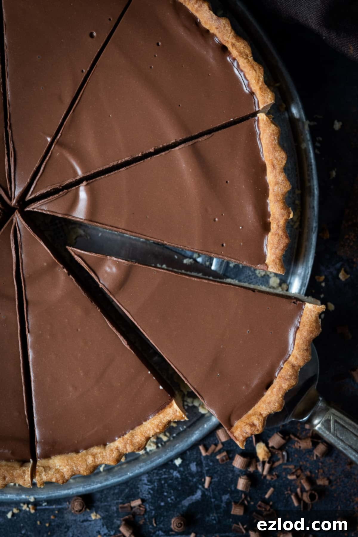 A slice of vegan chocolate peanut butter tart being carefully lifted from the main tart with a serving spatula, ready to be enjoyed.