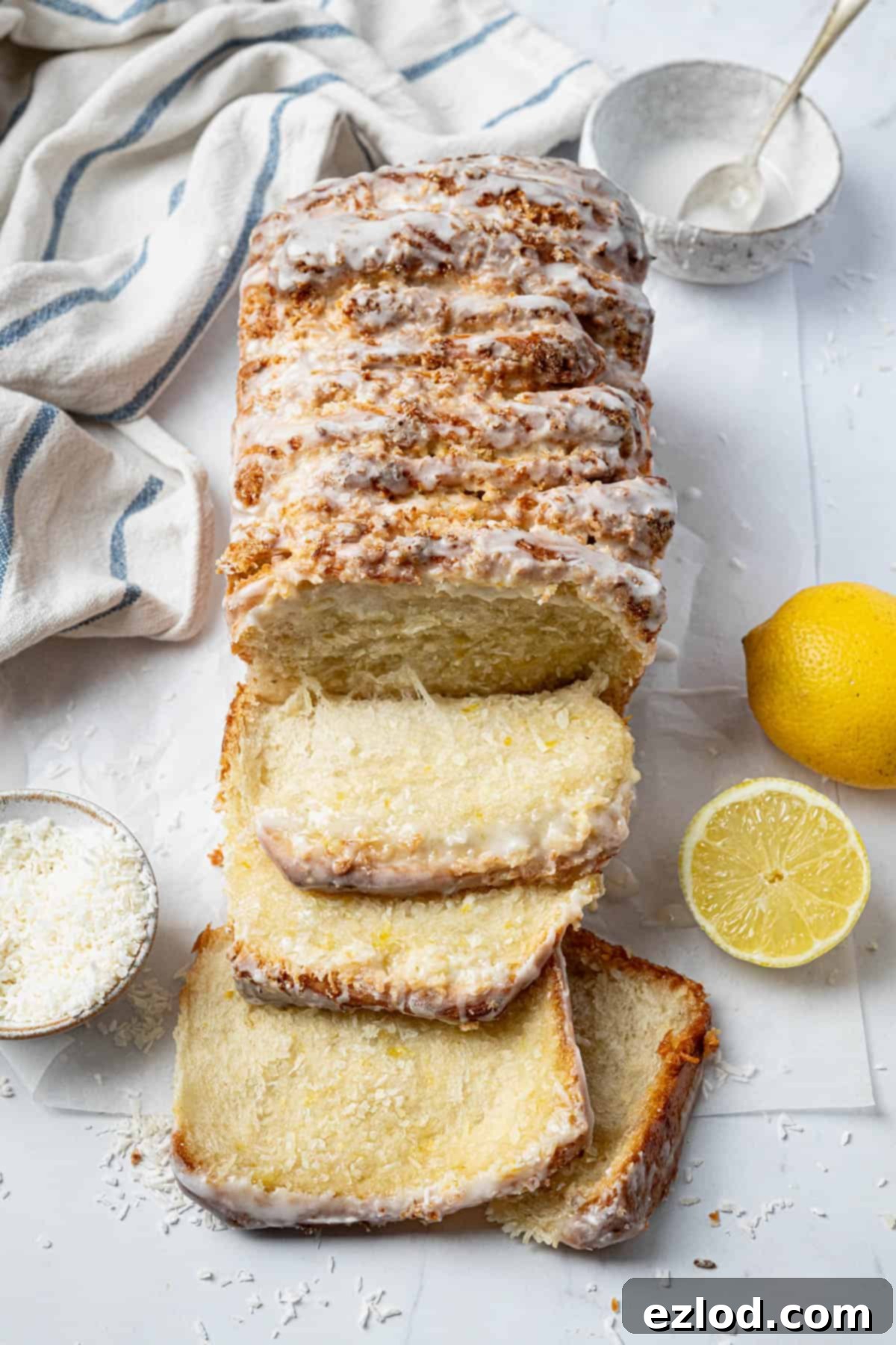 Vegan lemon coconut pull-apart bread on a sheet of baking paper with bowls of coconut and icing and some fresh lemons.