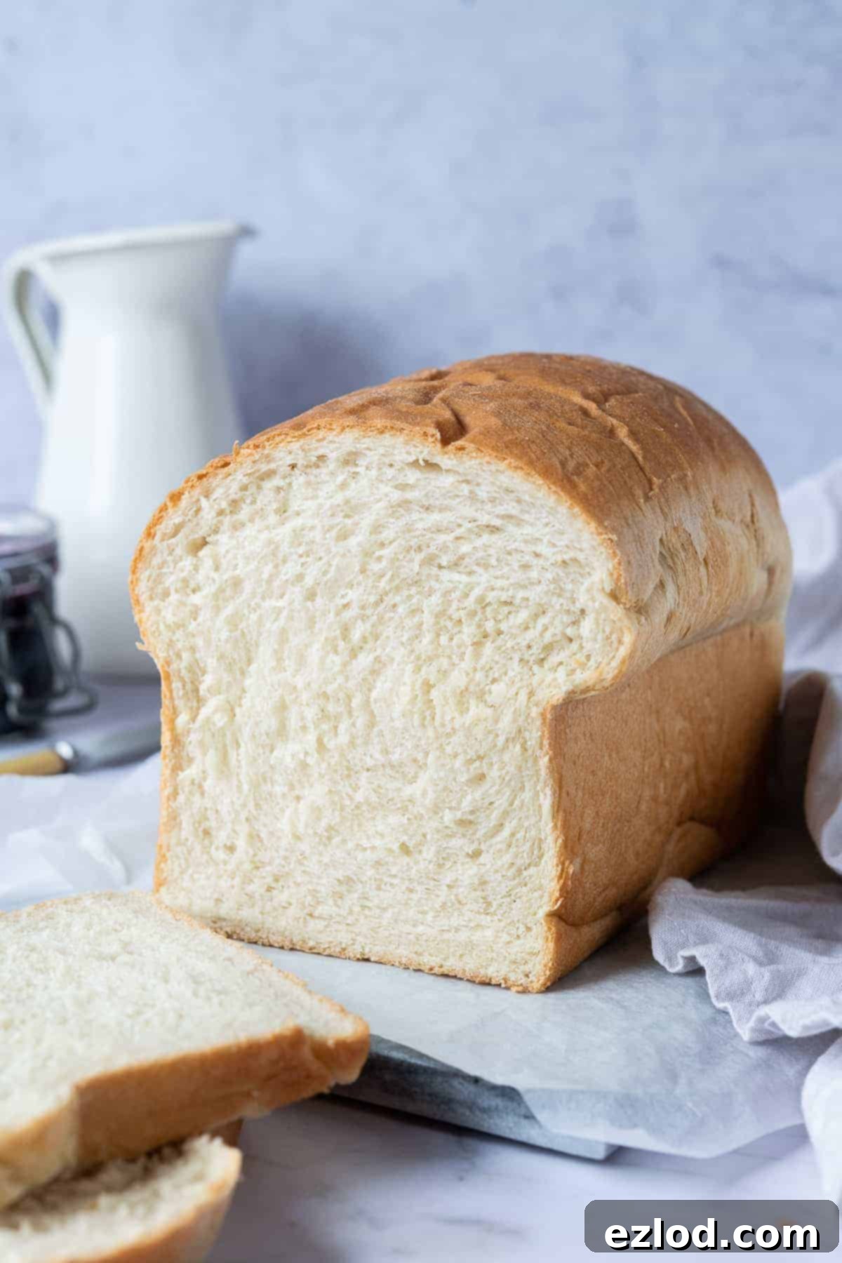 A loaf of vegan sandwich bread on a marble board with a white jug and a jar of jam.